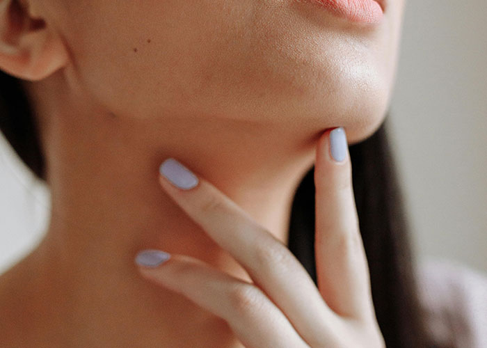 Close-up of a woman’s lower face and neck with fingers touching the skin, highlighting cosmetic procedure concerns.