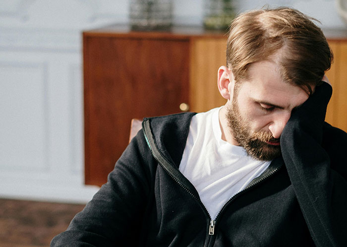 Man with beard and black hoodie looking down, appearing distressed, illustrating common mental health myths debunked by psychologists.