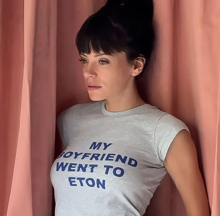 Woman wearing a t-shirt standing by pink curtains, related to fans clash online over David Harbour cheating controversy.