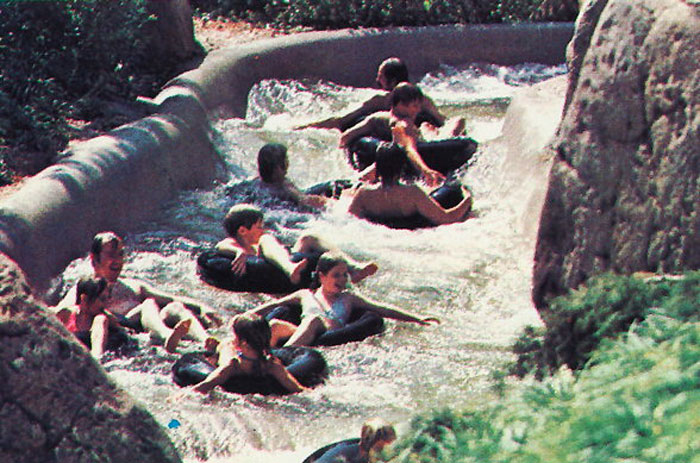 Visitors on a water ride at Disney World navigating rapids on inner tubes in a crowded, fast-moving attraction.