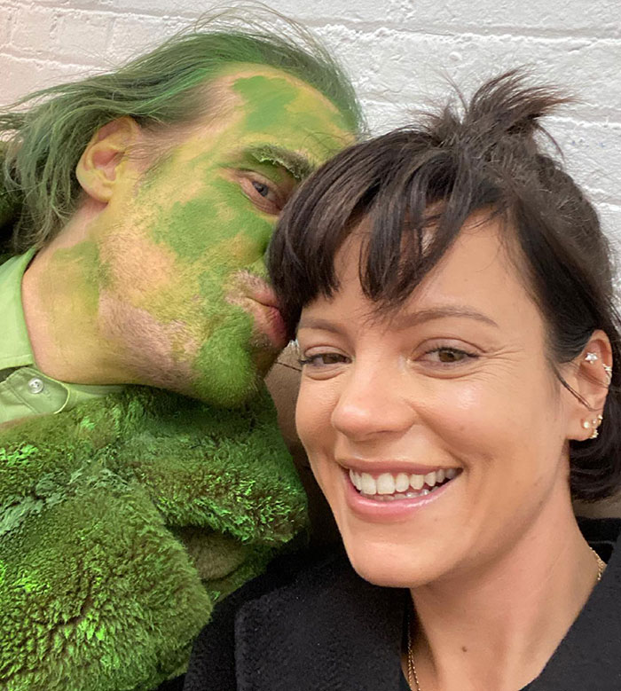 David Harbour and woman half his age posing together, with his face covered in green paint, in a candid close-up selfie.