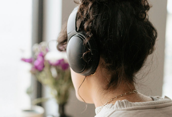 Woman wearing black headphones listening intently near a window with blurred flowers, illustrating one-in-a-million coincidences concept.