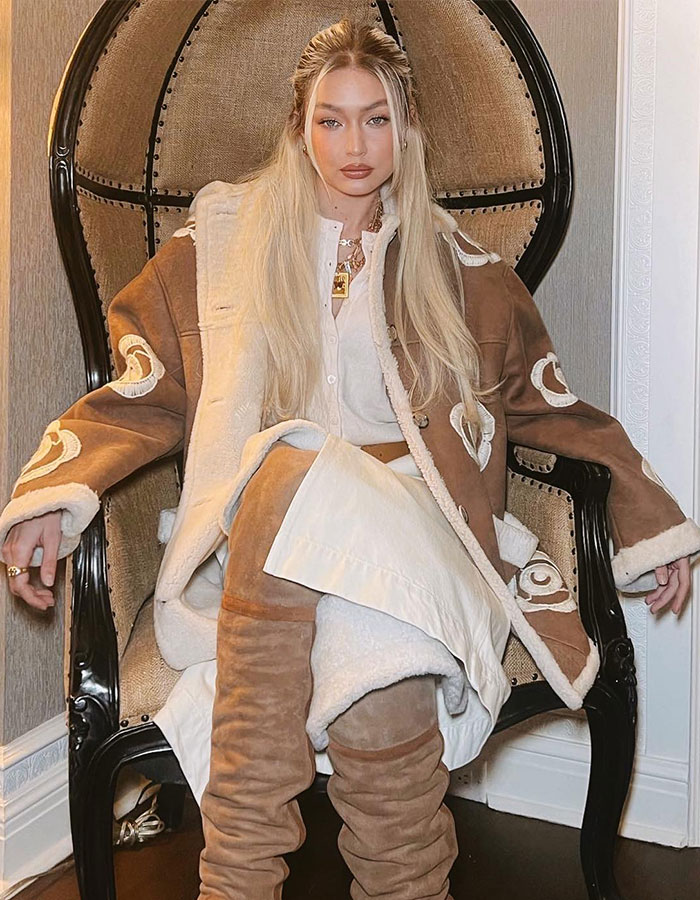 Fashionable celeb in beige and brown outfit sitting confidently on a large vintage chair, highlighting tone-deaf celebrity behavior.