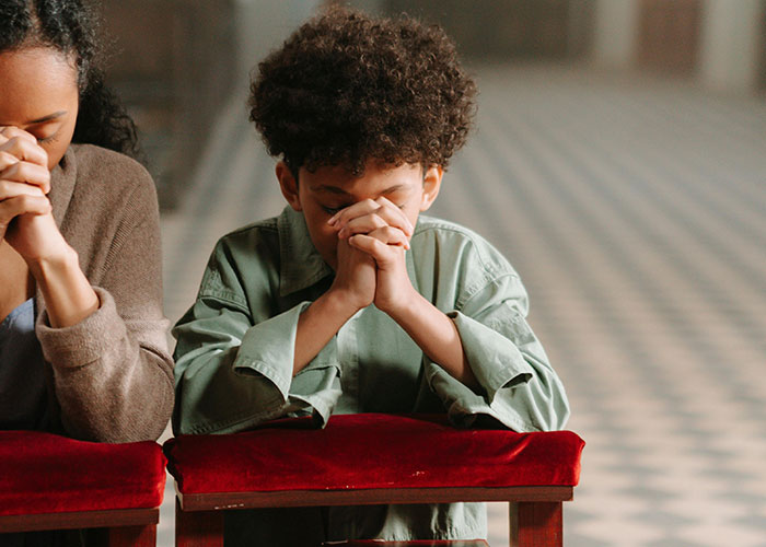 A mom and her child sitting on red cushions, heads bowed and hands clasped, sharing an emotional moment together.