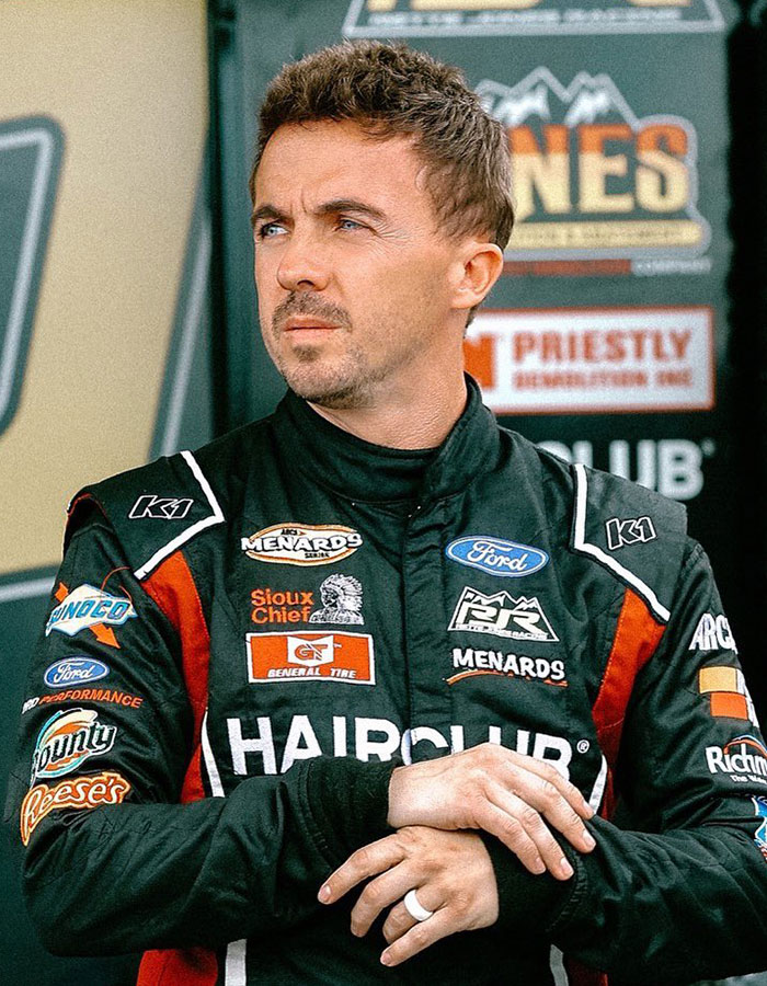 Race car driver in a sponsored suit representing famous men who are much shorter than fans imagined at an event.