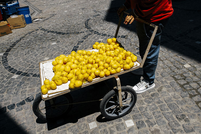 Person pushing cart full of lemons on a cobblestone street, capturing stunning street photography moments.
