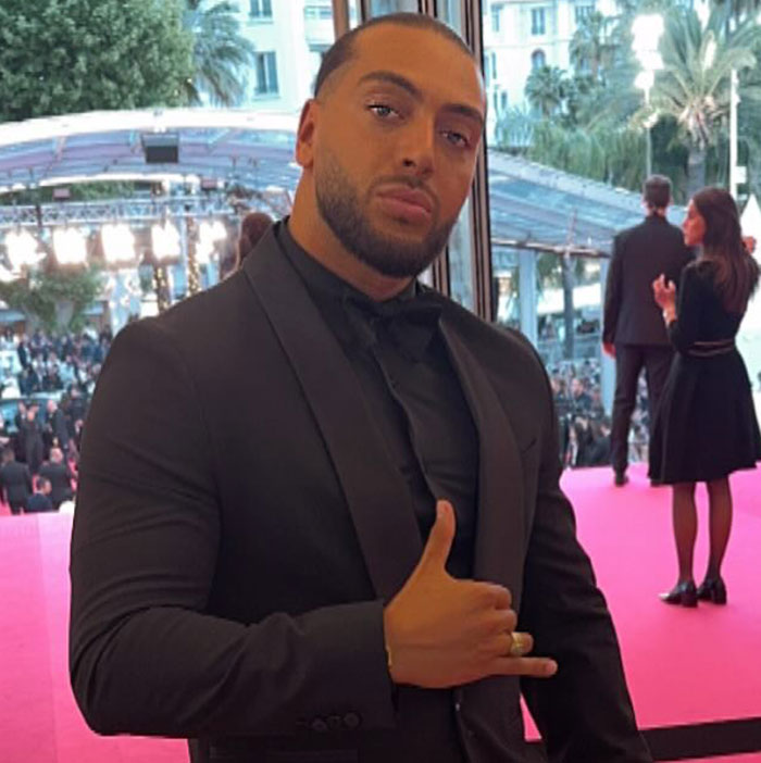 Man in black suit making a hand gesture at an event related to influencer's fake syringe attack pranks and arrest controversy.