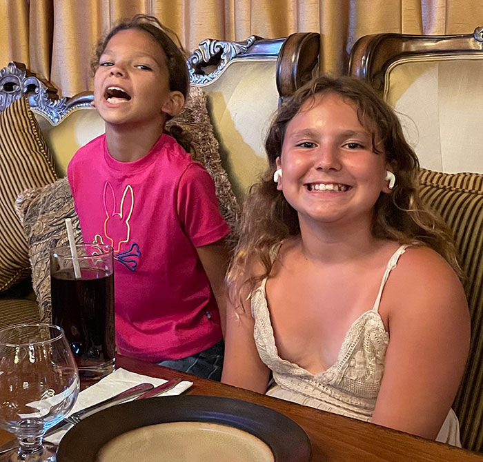 Two young girls smiling and sitting at a table, related to 12YO who lost her life subway surfing story.