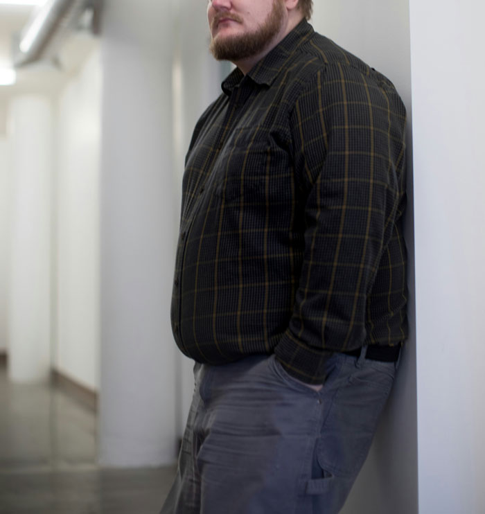 Bearded man in plaid shirt leaning against a wall, illustrating discussions on plastic surgeons and unnecessary surgeries.