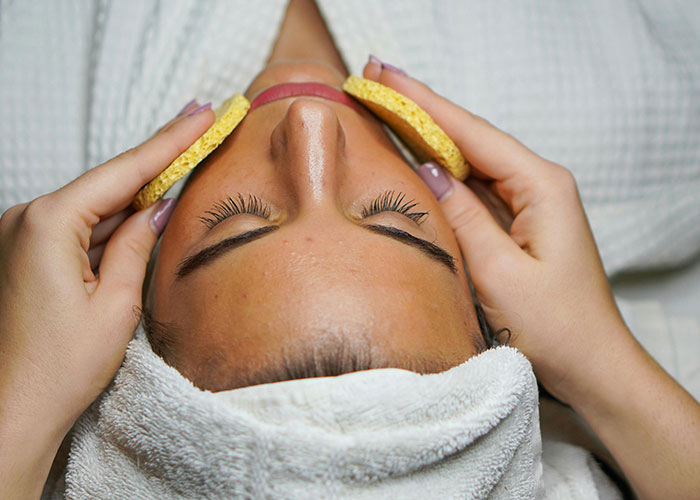 Close-up of a woman’s face receiving a cosmetic procedure with sponges during a facial treatment session.