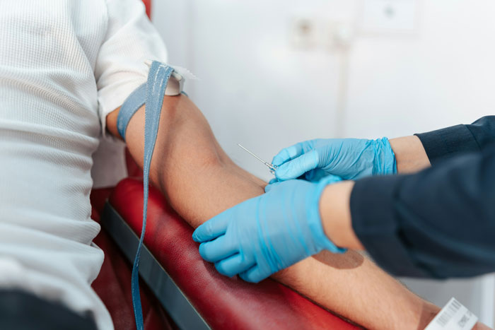 Person receiving blood draw from healthcare worker wearing gloves in medical setting, illustrating crimes related to hometown incidents.