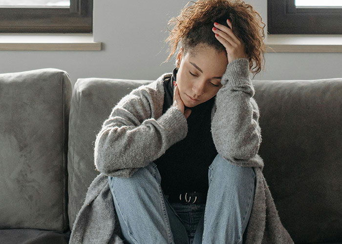 Young woman sitting on couch with hand on forehead, portraying mental health challenges and thoughtful reflection.