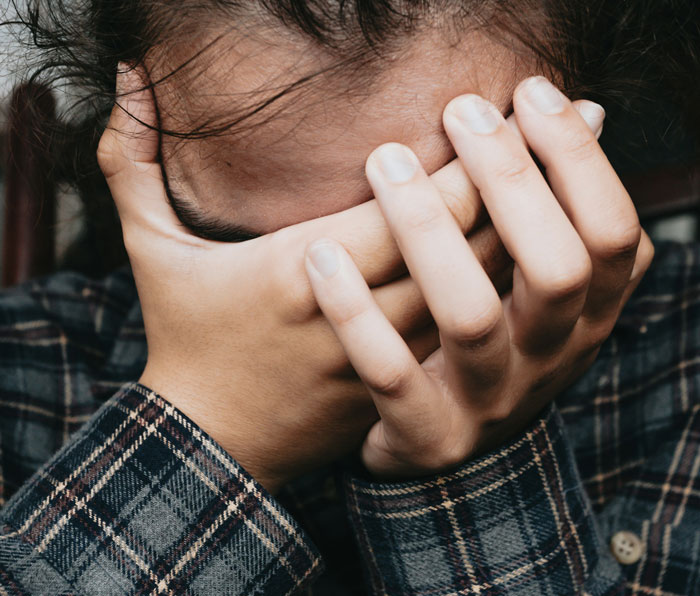 Stressed person covering face with hands, illustrating frustration dealing with worst employees in a workplace setting.