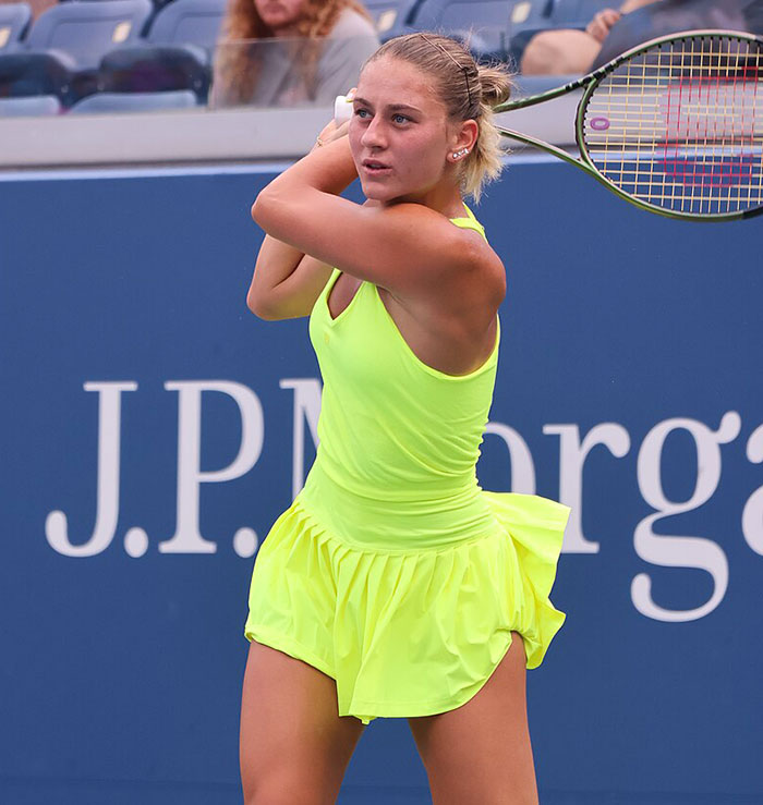 Female tennis player in bright yellow outfit preparing to hit a backhand during a professional match scene.