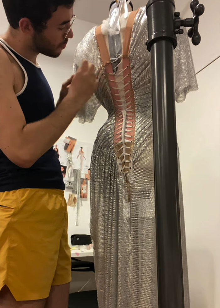 Fashion designer adjusting the laced back of Sydney Sweeney&rsquo;s gravity-defying dress on a mannequin in a studio.