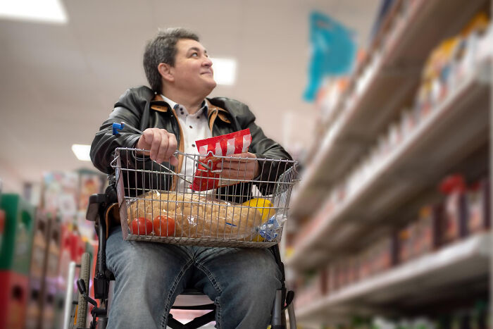 Person with disabilities shopping in a wheelchair, facing grocery store shelves, highlighting challenges faced daily.
