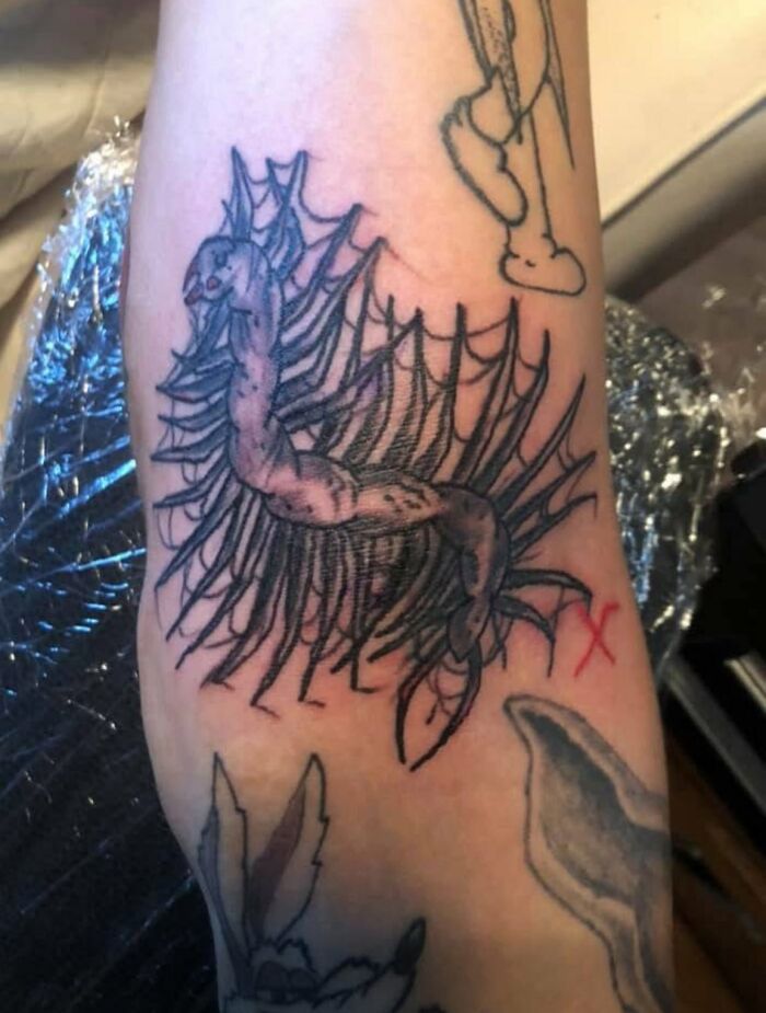 Unusual tattoo of a centipede-like creature with a distorted body and multiple legs on a person's arm, unusual tattoos.