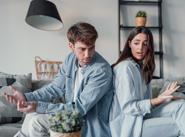 Couple arguing on a couch with woman refusing to contribute to bills after boyfriend spends heavily on house purchase.