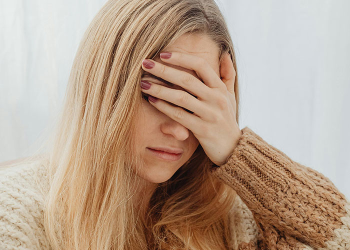 Woman in a cozy sweater covering her face, feeling embarrassed and emotional about a kid embarrassing moment shared by moms.