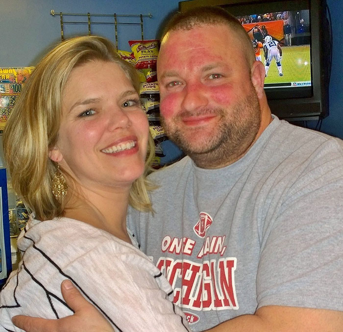 Couple smiling and hugging indoors with television and snack display in background, related to morbidly obese patient and dentist.
