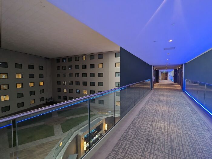 Modern hotel corridor with blue lighting and glass railing overlooking an unnerving liminal space at night