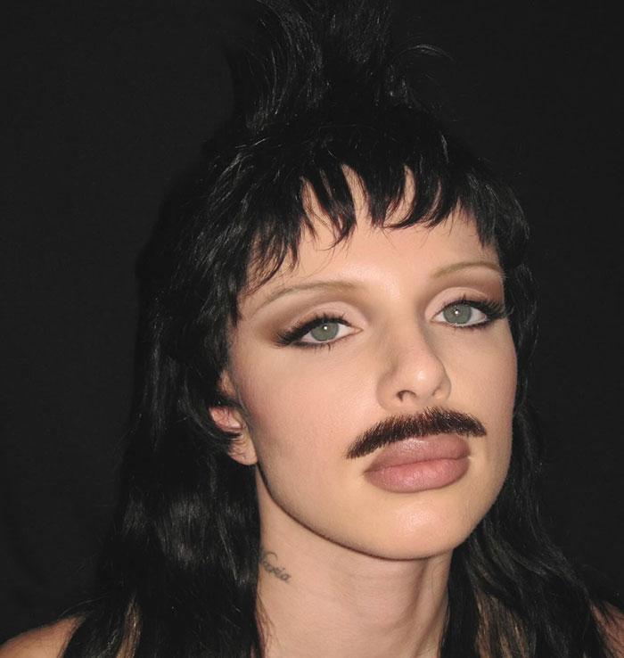 Person with a mustache and dark hair styled upwards, showcasing a desperate look related to Julia Fox's barely-there dress.