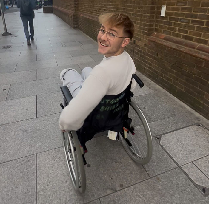 Young man in wheelchair outdoors, smiling, discussing leg amputation after attending a rock concert experience.