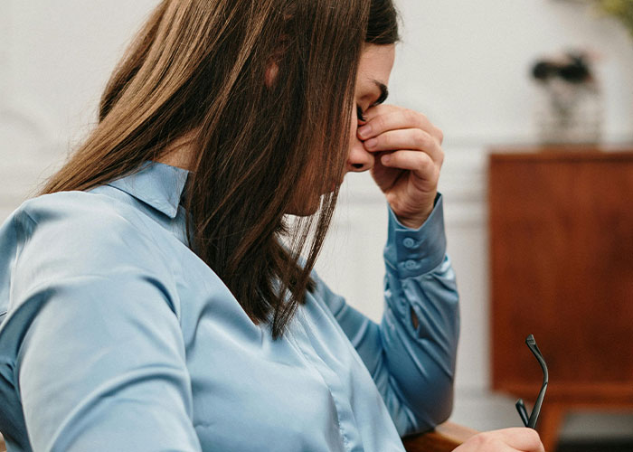 Woman in a blue shirt holding glasses and pinching bridge of nose, illustrating mental health myths debunked by psychologists.