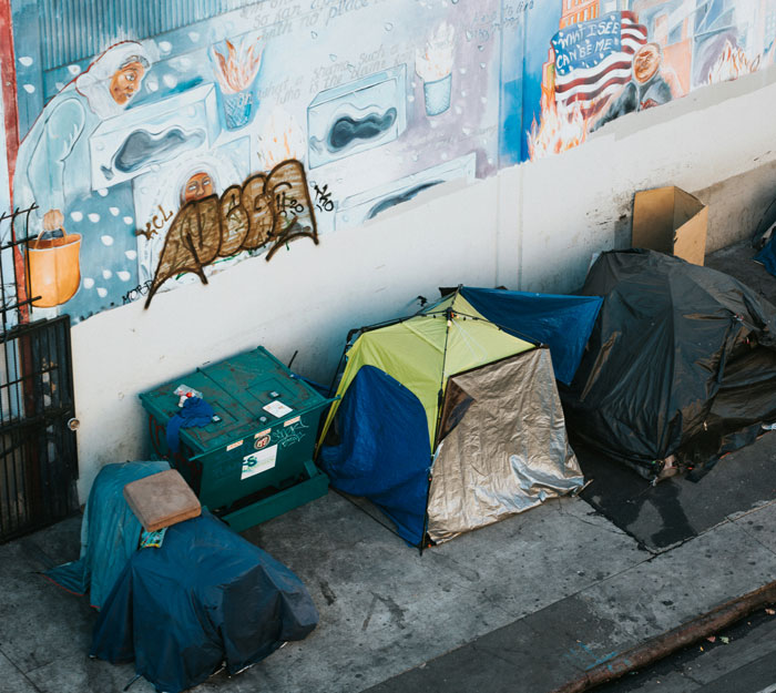 Homeless tents lined up against a graffiti-covered wall, illustrating places people wouldn’t revisit.