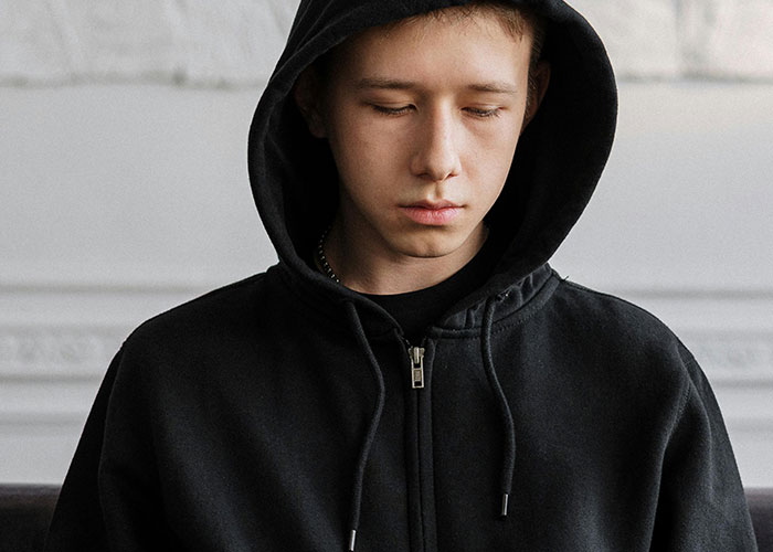Young man in a black hoodie looking down, reflecting on creepy things women said or did that left men horrified.