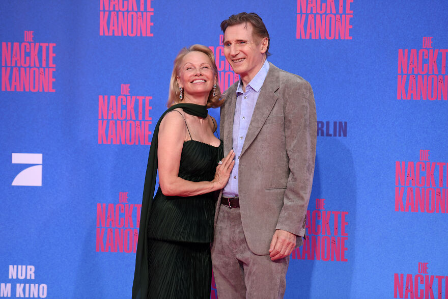 Pamela Anderson and Liam Neeson posing on red carpet event with backdrop, related to Pamela Anderson's net worth and decades of reinvention.