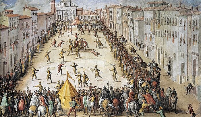 Crowd watching a dangerous and unsafe historical sports event in a large open square with players and horses.
