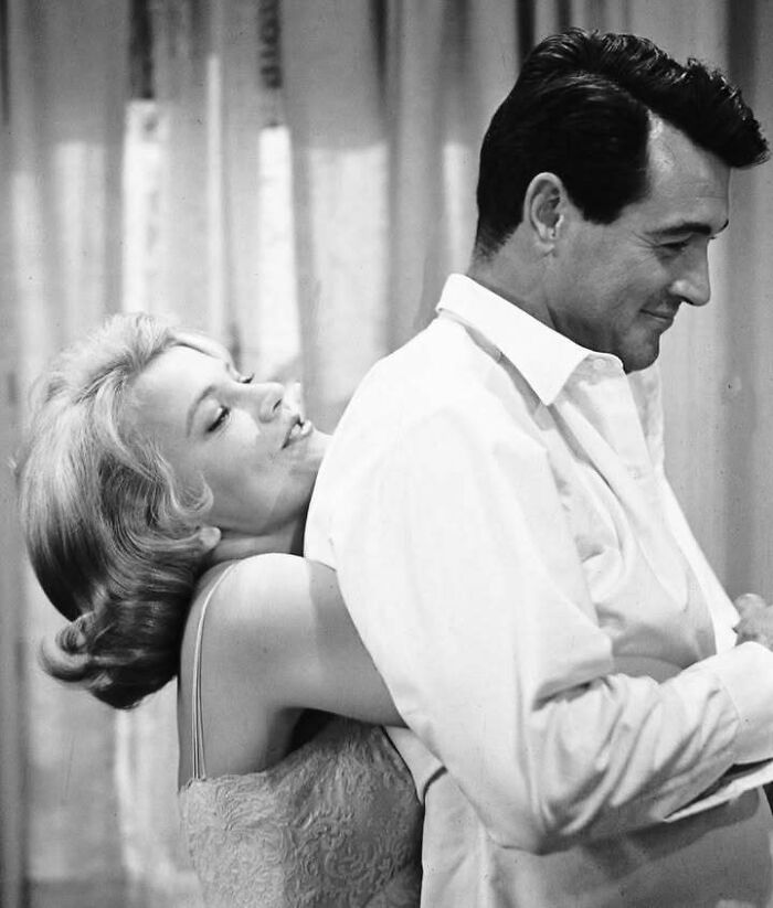 Black and white image of a woman embracing a man, representing iconic people who left a mark in movie and music industries.