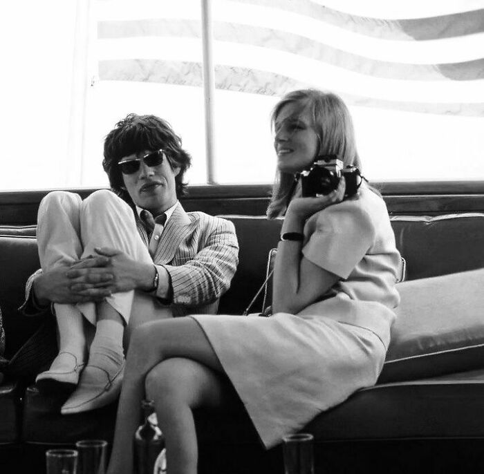 Black and white photo of two people relaxing on a couch holding a camera, representing stories about movie and music industries.