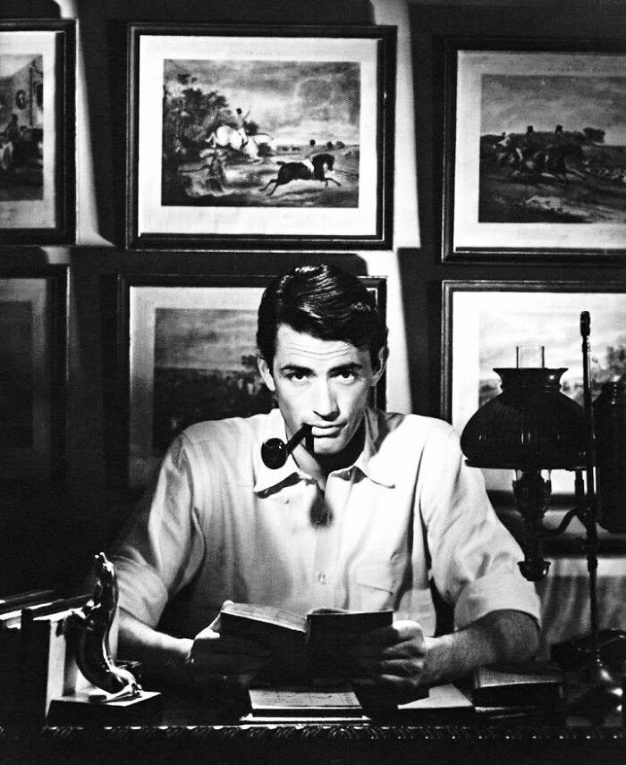 Black and white photo of a man reading a book with a pipe in his mouth, reflecting impact in movie and music industries.