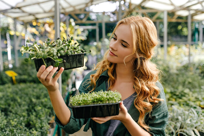 Woman in a greenhouse holding trays of seedlings, illustrating life hacks that trick people into doing extra work.