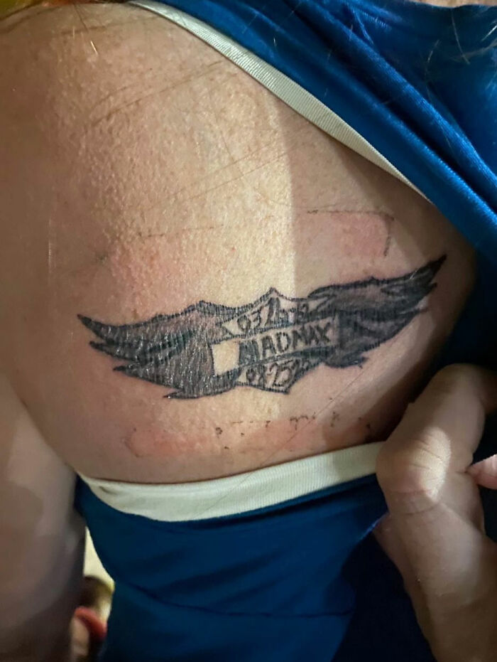 Tattoo of black wings and a shield with text on a person's upper back, an unusual design from 91 tattoos collection.