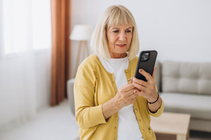 Elderly woman with poor technology skills holding a smartphone, illustrating parents being bad at technology skills in a funny moment.