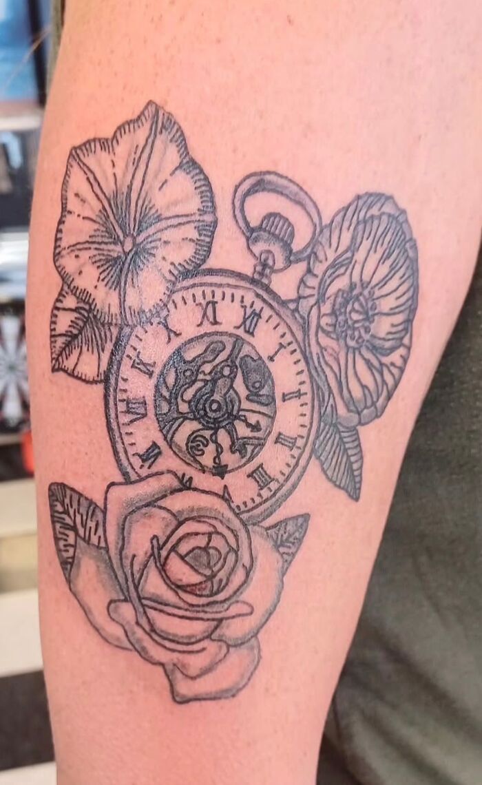 Black and grey tattoo of a vintage pocket watch surrounded by detailed flowers on a person's arm, unique body art design.