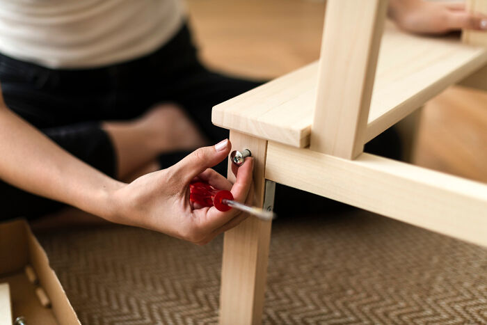 Person using a red screwdriver to assemble wooden furniture, illustrating practical moving advice for zip-line your boxes out.