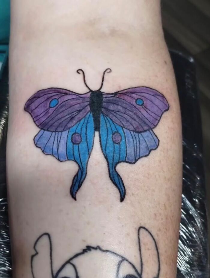 Colorful butterfly tattoo in purple and blue ink on a person's forearm, one of the unusual tattoos on bodies.