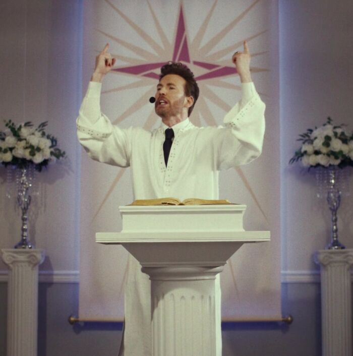Man in a white robe speaking passionately at a podium with a star design in the background during a church service.