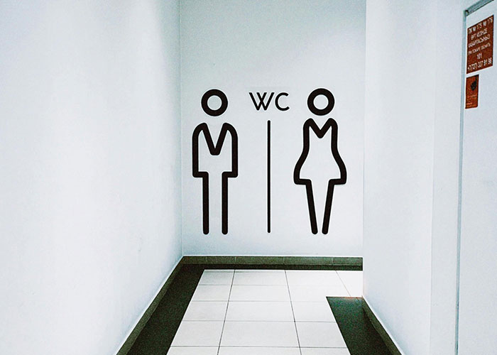 Restroom symbols on a white wall in a hallway, illustrating moments moms share about kids embarrassing them.