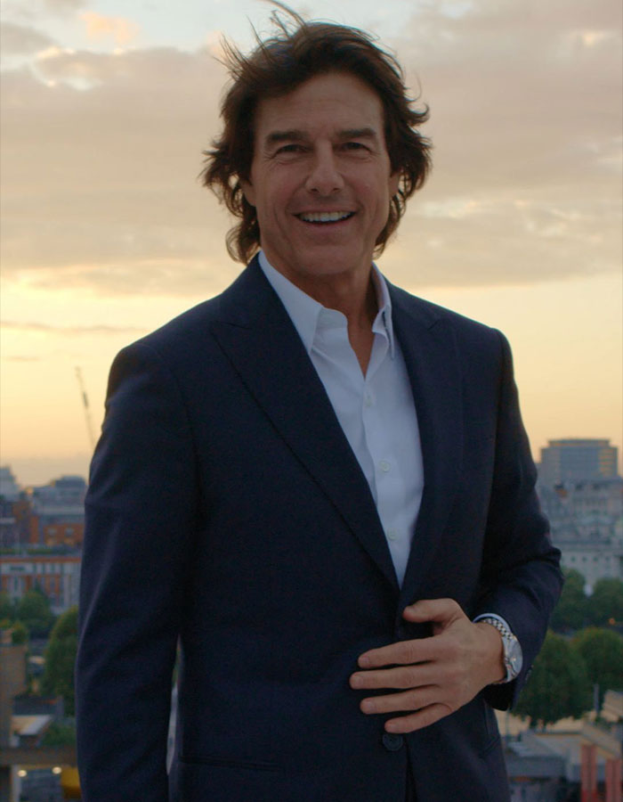 Tom Cruise smiling outdoors at sunset, dressed in a dark suit, one of the famous men shorter than fans imagined.