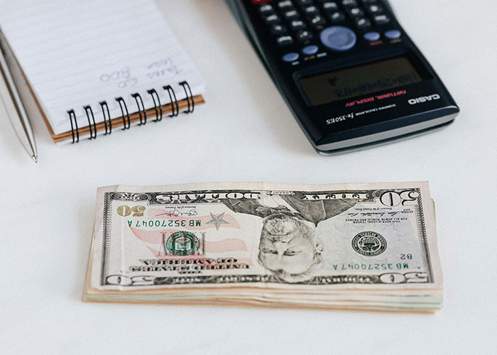 Stack of fifty dollar bills next to calculator and notebook illustrating life hacks for saving money accidentally discovered