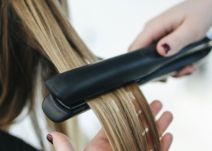 Close-up of a cosmetic procedure involving hair straightening with a flat iron on blonde hair strands.