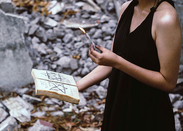 Woman in a black dress holding a burning candle and an ancient book with symbols, evoking creepy things women said or did.