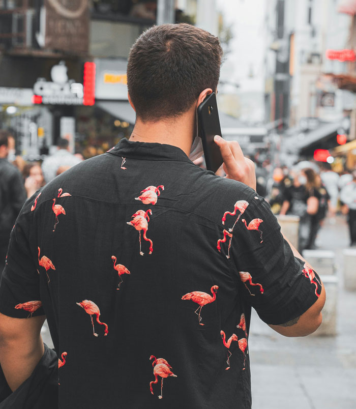 Man wearing a flamingo shirt talking on phone in busy street, symbolizing people who endured narcissistic mothers.