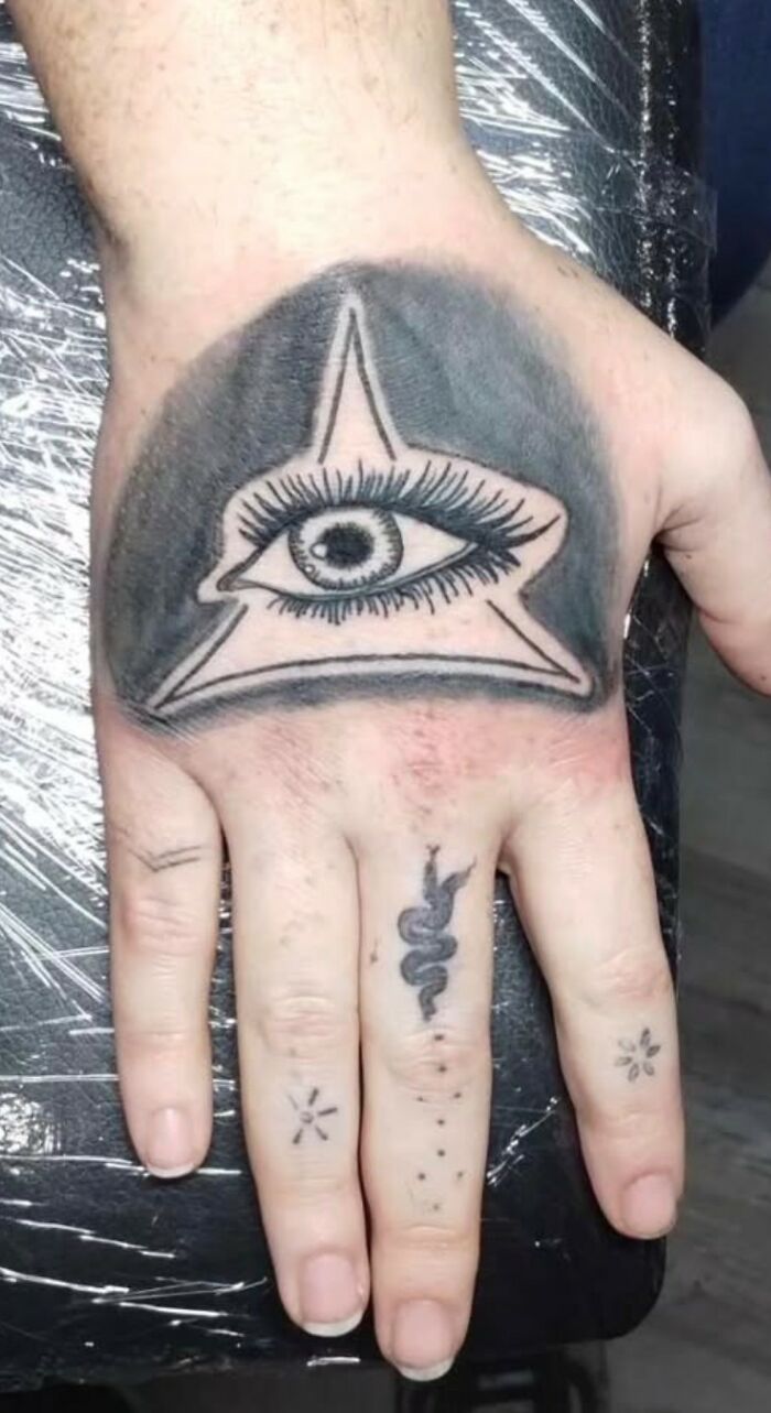 Tattoo of an eye inside a star on the hand with additional small tattoos on the fingers, part of unusual tattoos collection.