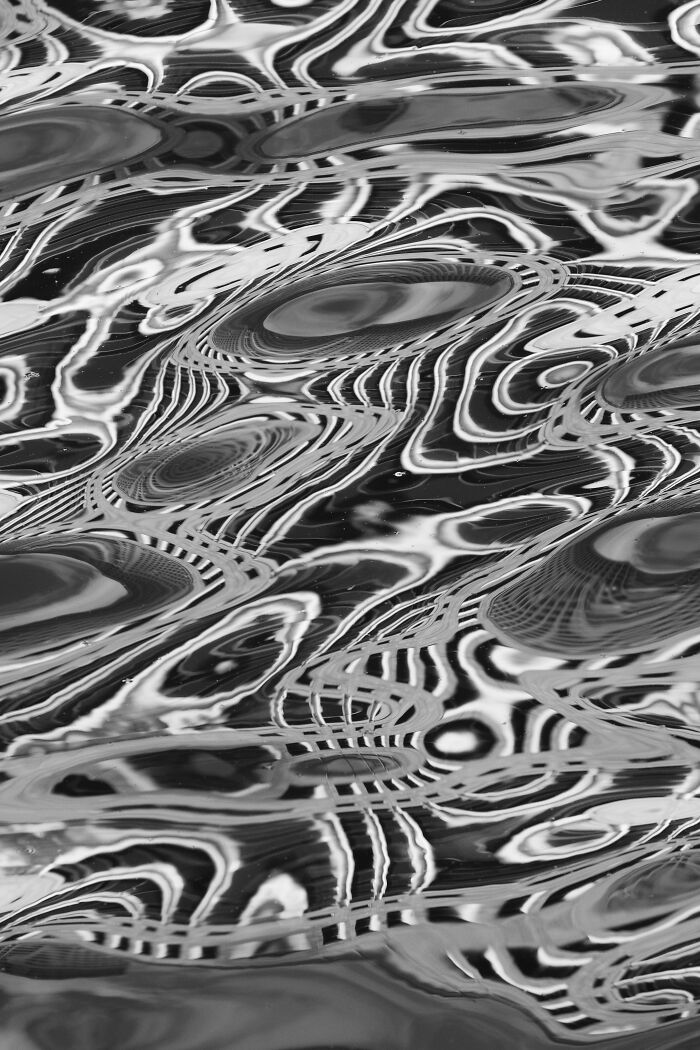 Black and white abstract pattern of distorted light reflections on water, showcasing street photography’s unexpected moments.